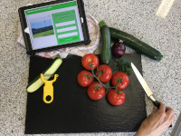 iPad, Schneidebrett, Hand die zum Messer greift und Gemüse