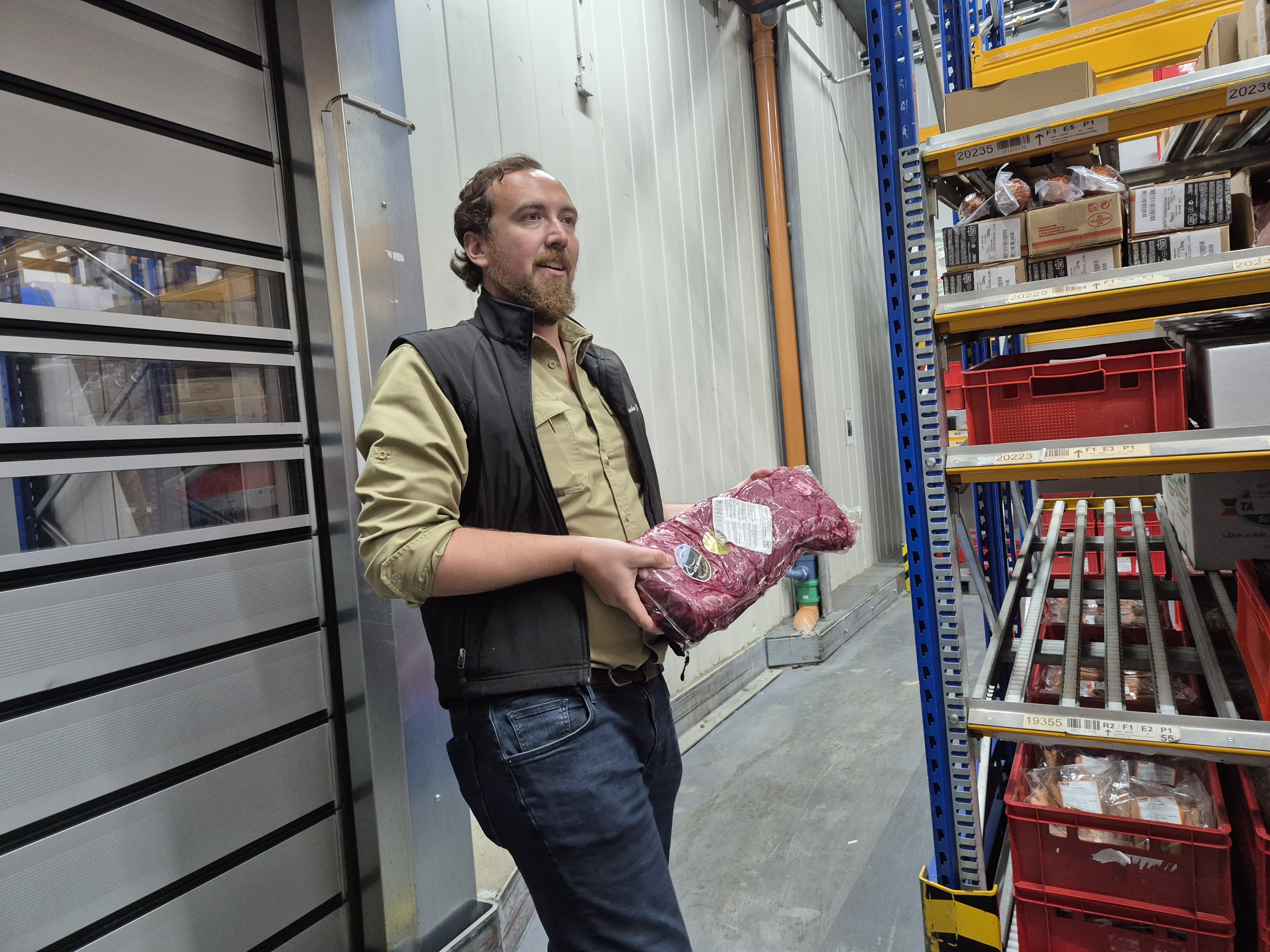 Maximilian Jork hält ein großes Roastbeefstück das einvakuumiert ist und zeigt es den Teilnehmenden (die nicht zu sehen sind)