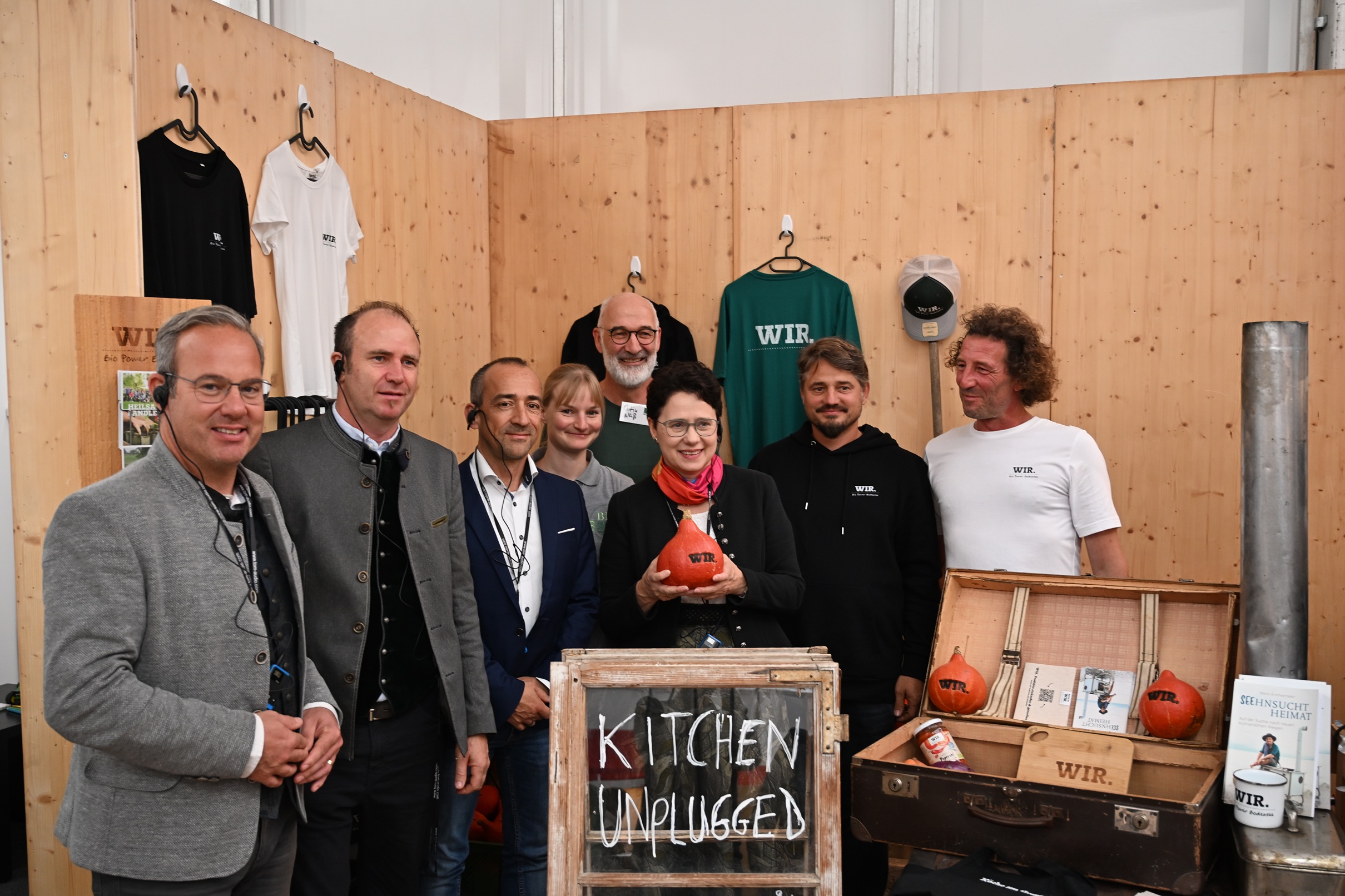 Ministerin Gentges steht umringt von sieben weiteren Personen an einem Stand und hält einen Kürbis auf dem WIR steht in die Kamera