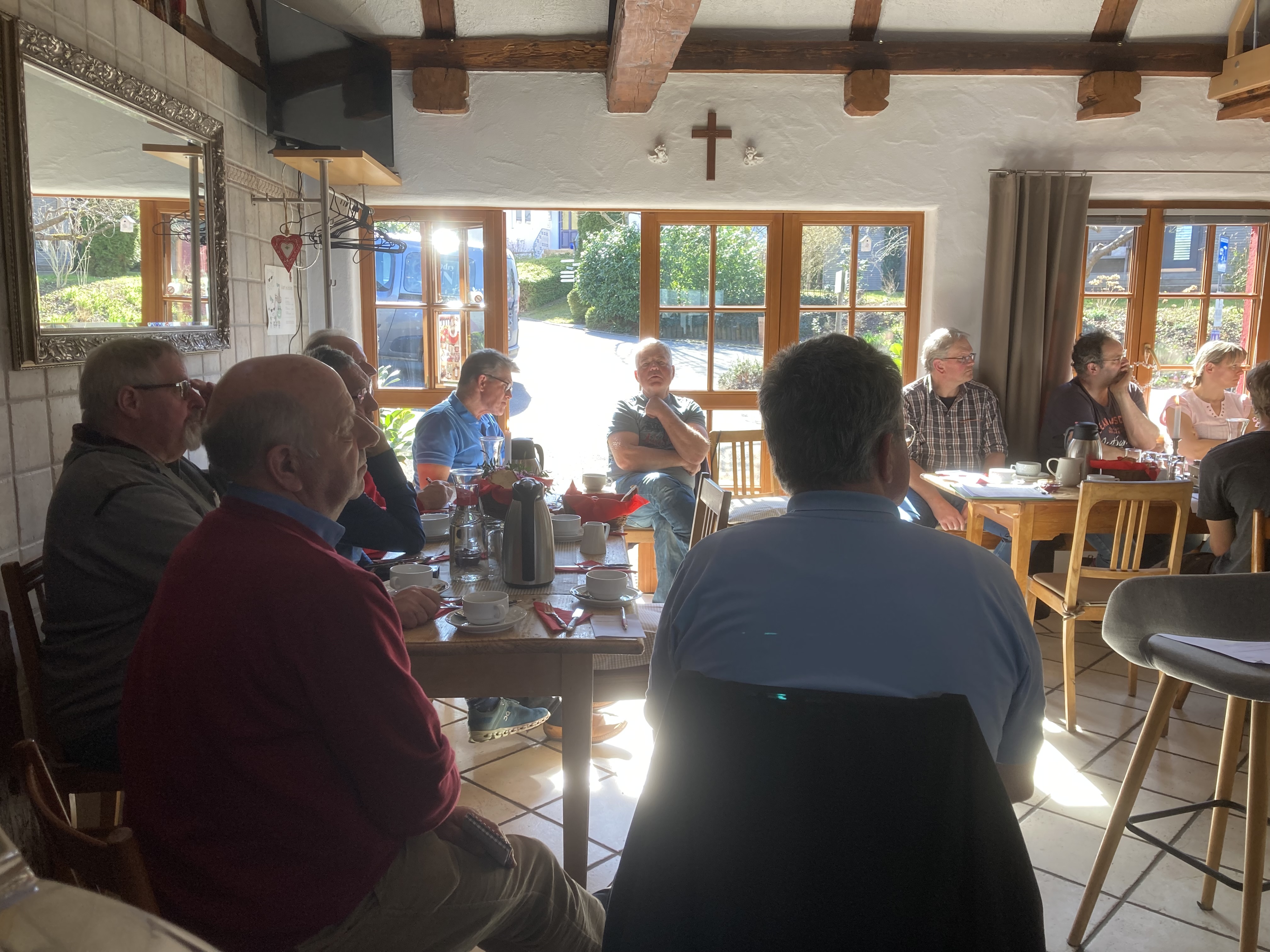 Teilnehmende der Mitgliederversammlung lauschen dem Vorstand und sitzen in einem urigen Gasraum eines Gasthausees. Draußen schein die Sonne. 
