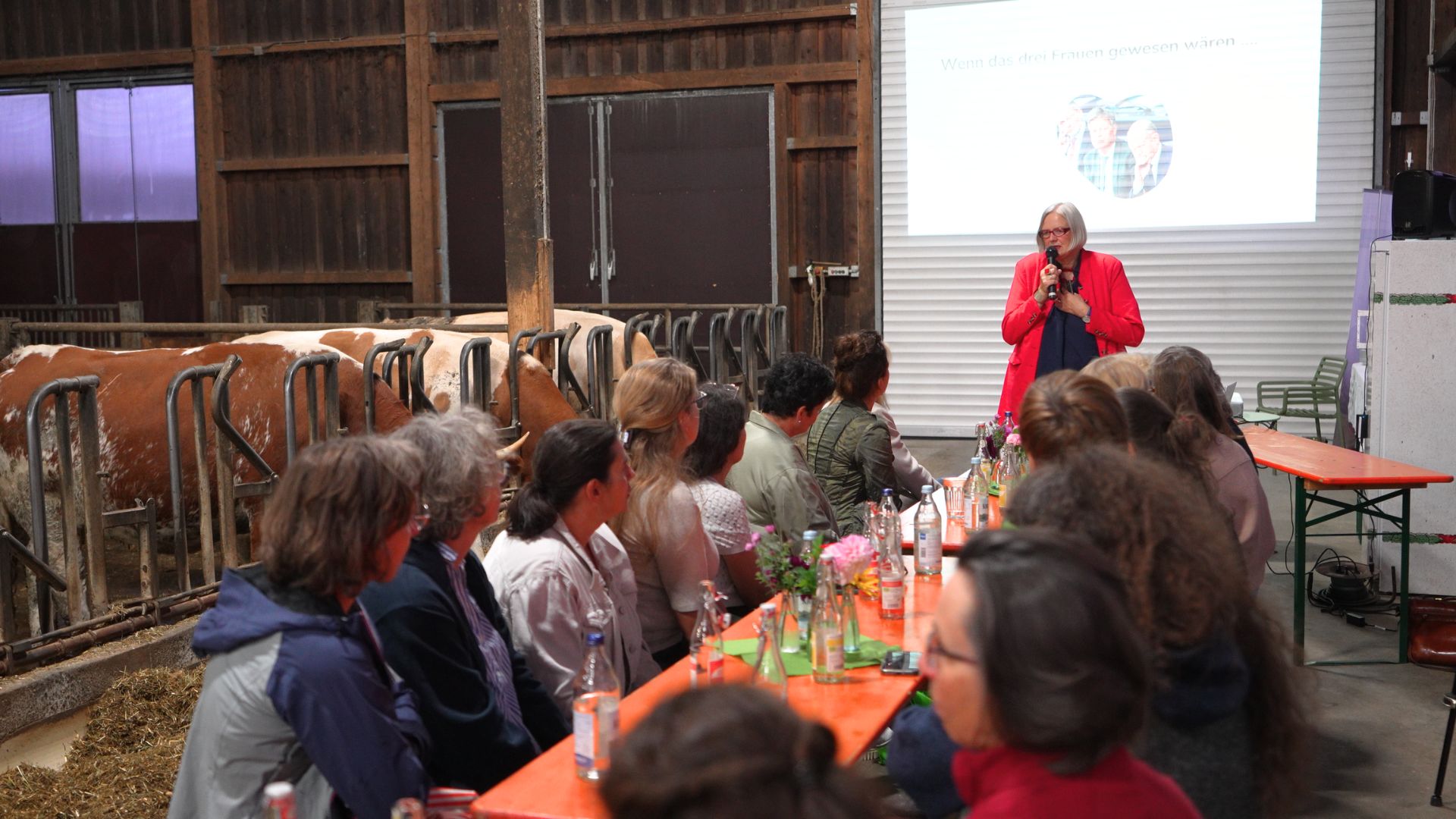 Eine Frau steht vor einer Tafel an der Frauen sitzen und referiert. Im Hintergrund sieht man ihre Folien hinter den Frauen sieht man die Kühe. 