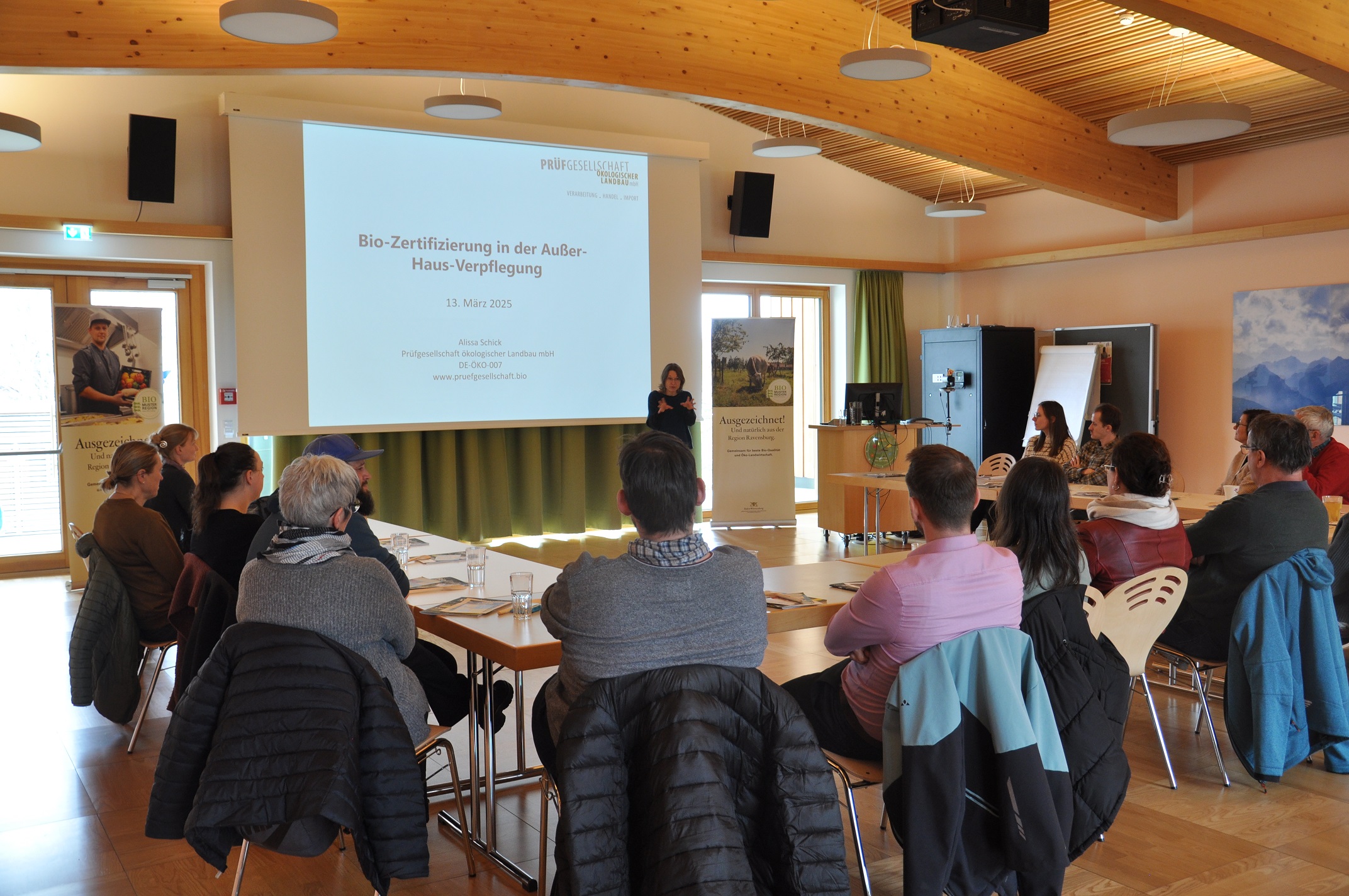 Teilnehmende sitzen im U und lauschen gespannt dem Vortrag von Alissa Schick die vorne neben der Leinwand mit ihren Folien zu sehen ist. 