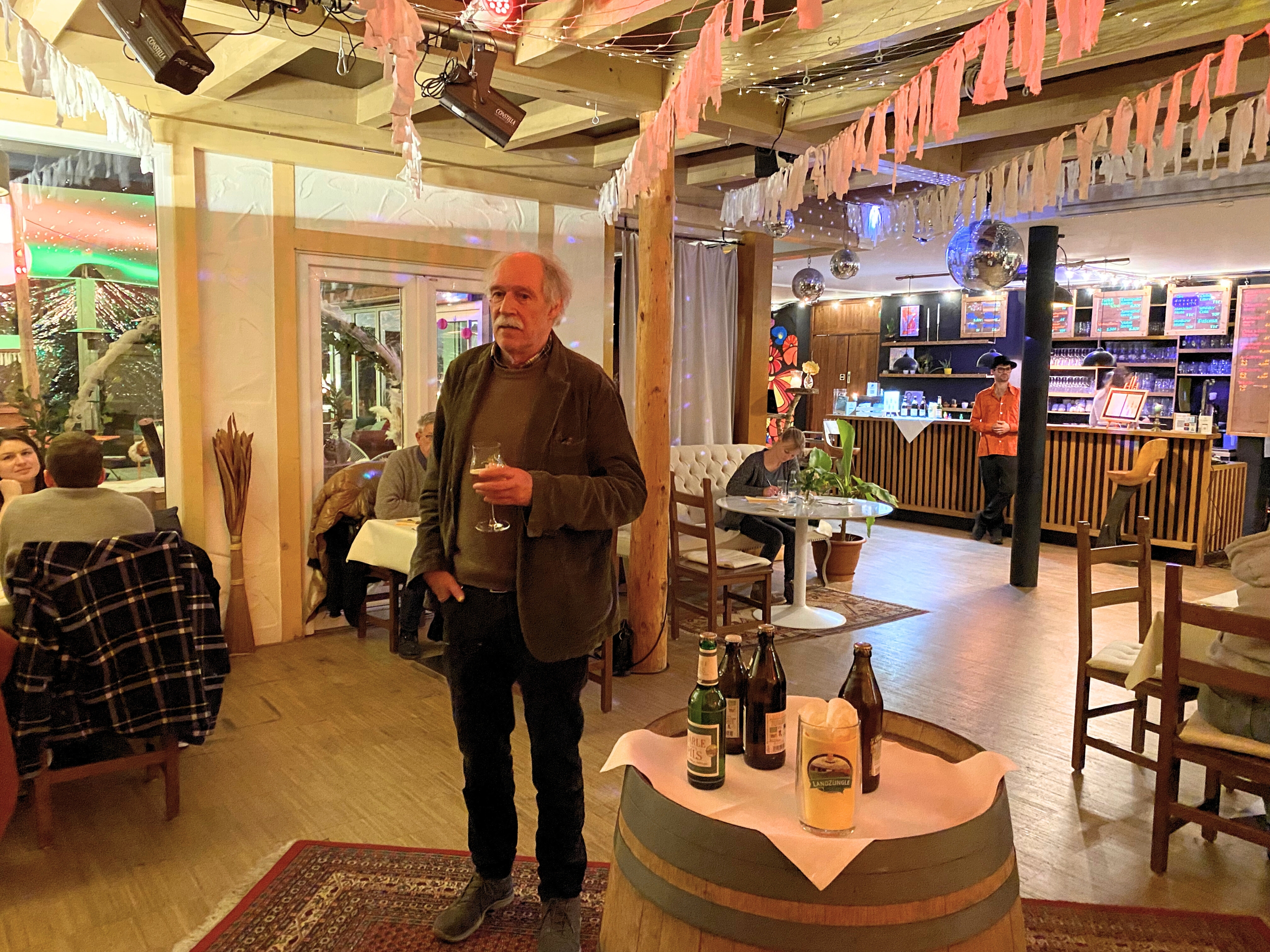 Gottfried Härle steht in der Mitte des Saales mit einem Bierglas in der Hand und spricht. Vor ihm steht ein Holzfass auf dem die fünf verschiedenen Biere des Abends stehen