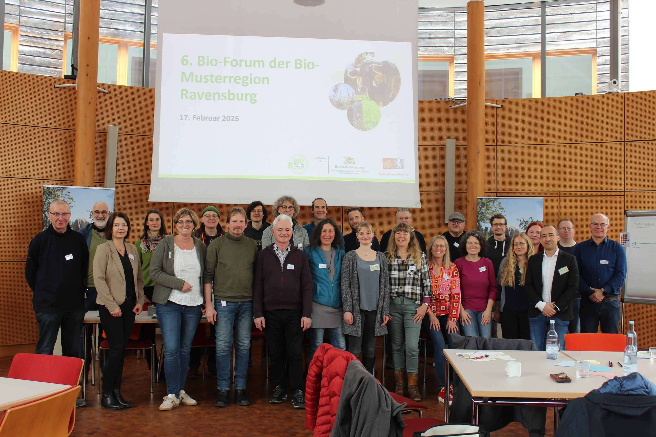 Teilnehmende des Bio-Forums stehen vor der Leinwand auf der das 6. Bio-Forum angekündigt ist